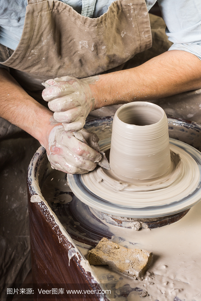 陶艺,作坊,陶艺艺术概念-一个男人的手与陶工的车轮,手指形成形状的生火粘土,男性大师雕刻器具与海绵和雕刻工具,俯视图,垂直